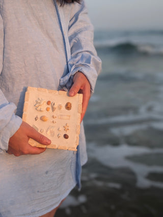 Cadre en travertin avec coquillages tenu dans les mains, bord de mer